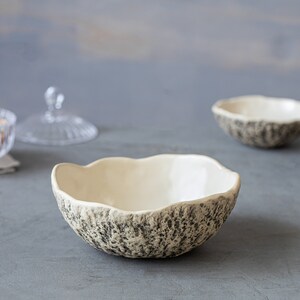 May include: Three white ceramic bowls with a textured, gray and white speckled exterior. The bowls are sitting on a gray surface.