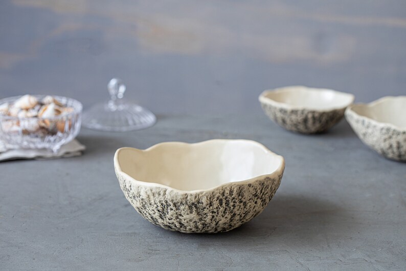 May include: Three white ceramic bowls with a textured, gray and white speckled exterior. The bowls are sitting on a gray surface.