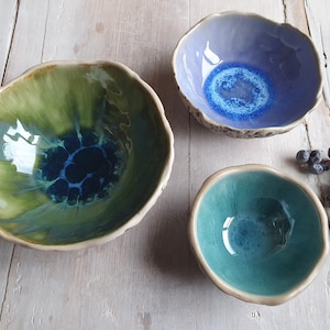 May include: Three ceramic bowls in different sizes and colours. The largest bowl is green with blue and white accents. The medium bowl is purple with blue accents. The smallest bowl is teal.