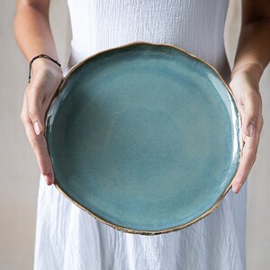 May include: A large, round, light blue ceramic plate with a slightly uneven, golden rim.