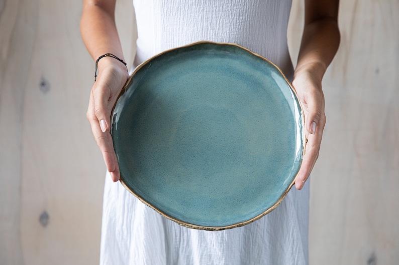 May include: A large, round, light blue ceramic plate with a slightly uneven, golden rim.