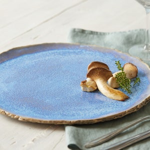 May include: A blue ceramic plate with a rough, textured rim. Three mushrooms are arranged on the plate with a sprig of thyme.