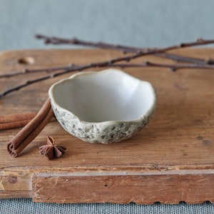 May include: A small white ceramic bowl with a textured exterior sits on a wooden chopping board with two cinnamon sticks and a star anise.