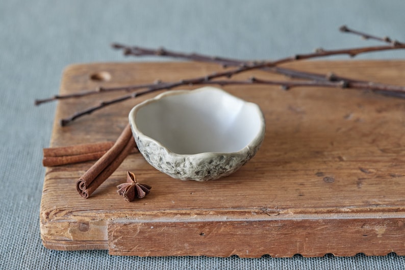 May include: A small white ceramic bowl with a textured exterior sits on a wooden chopping board with two cinnamon sticks and a star anise.