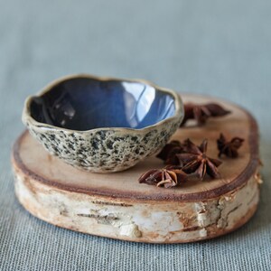 May include: A small, blue and white speckled ceramic bowl with a wavy rim sits on a wooden slice with star anise pods scattered around it.