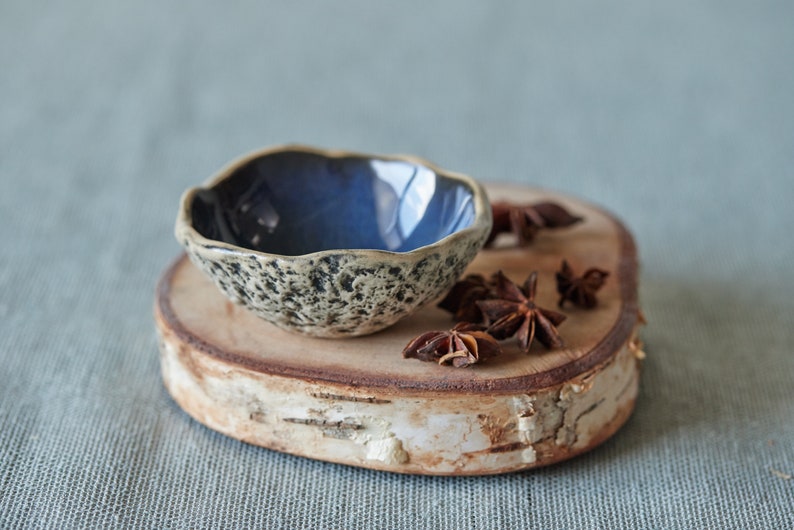 May include: A small, blue and white speckled ceramic bowl with a wavy rim sits on a wooden slice with star anise pods scattered around it.