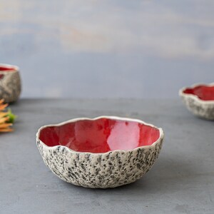May include: A set of three red ceramic bowls with a textured white exterior. The bowls are handmade and have a unique, organic shape.
