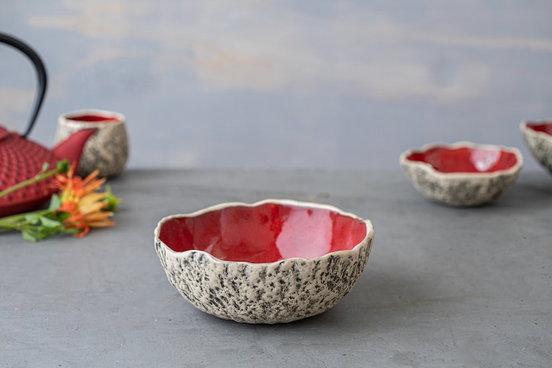 May include: A set of three red ceramic bowls with a textured white exterior. The bowls are handmade and have a unique, organic shape.