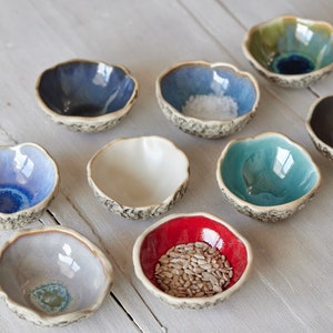 May include: Set of ten small ceramic bowls in various colours, including blue, green, white, red, and grey. The bowls have a textured, rustic look and are perfect for serving small snacks or condiments.