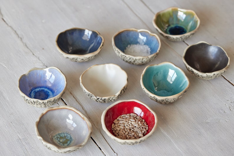 May include: Set of ten small ceramic bowls in various colours, including blue, green, white, red, and grey. The bowls have a textured, rustic look and are perfect for serving small snacks or condiments.