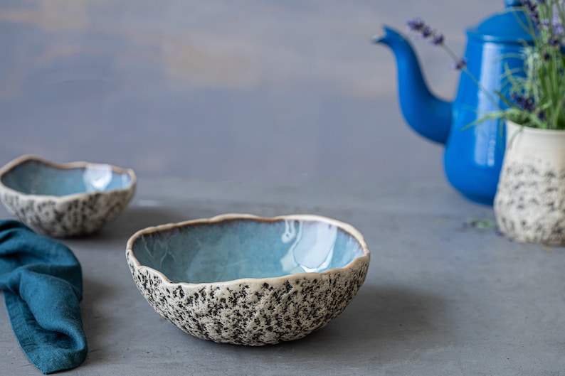 May include: Two blue and white ceramic bowls with a textured exterior. The bowls are on a gray surface.