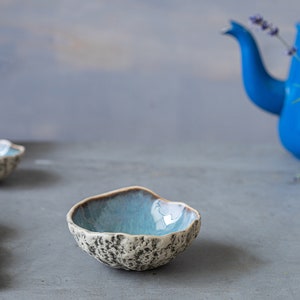K&ouml;nnte beinhalten: Drei kleine blaue und wei&szlig;e Keramikschalen mit einer strukturierten Oberfl&auml;che. Die Schalen sind auf einer grauen Oberfl&auml;che angeordnet. Im Hintergrund befinden sich eine blaue Teekanne und eine wei&szlig;e Vase mit einer strukturierten Oberfl&auml;che.