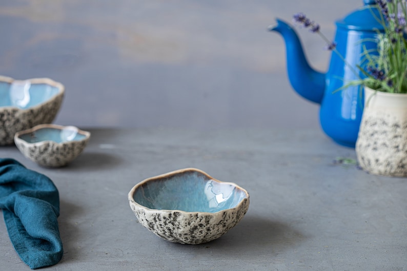 K&ouml;nnte beinhalten: Drei kleine blaue und wei&szlig;e Keramikschalen mit einer strukturierten Oberfl&auml;che. Die Schalen sind auf einer grauen Oberfl&auml;che angeordnet. Im Hintergrund befinden sich eine blaue Teekanne und eine wei&szlig;e Vase mit einer strukturierten Oberfl&auml;che.