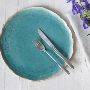 May include: A teal ceramic plate with a rough, textured edge. A silver fork and knife are placed on the plate.