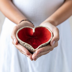 Puede incluir: Una persona sosteniendo un taz&oacute;n de cer&aacute;mica en forma de coraz&oacute;n con un esmalte rojo y un exterior blanco moteado.