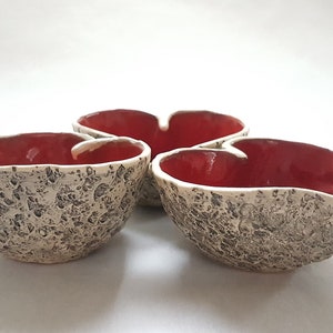 May include: Three ceramic heart-shaped bowls with a textured exterior and a red glaze on the inside.