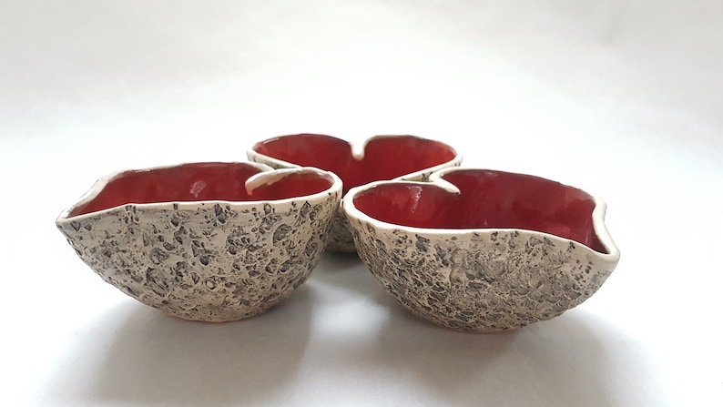 May include: Three ceramic heart-shaped bowls with a textured exterior and a red glaze on the inside.