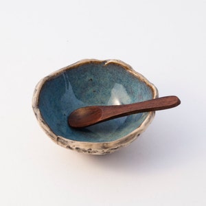 May include: A small, blue ceramic bowl with a rough, textured exterior and a wooden spoon resting inside.