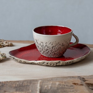May include: A red and white ceramic teacup and saucer set. The cup has a textured exterior and a red interior. The saucer is red with a textured edge.