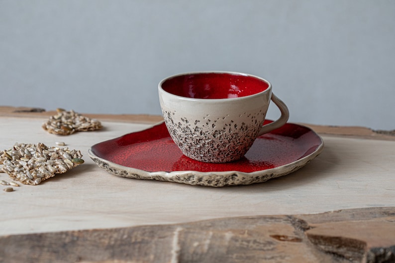 May include: A red and white ceramic teacup and saucer set. The cup has a textured exterior and a red interior. The saucer is red with a textured edge.