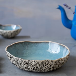 May include: A set of three blue and white ceramic bowls with a textured exterior. The bowls are arranged on a gray surface.
