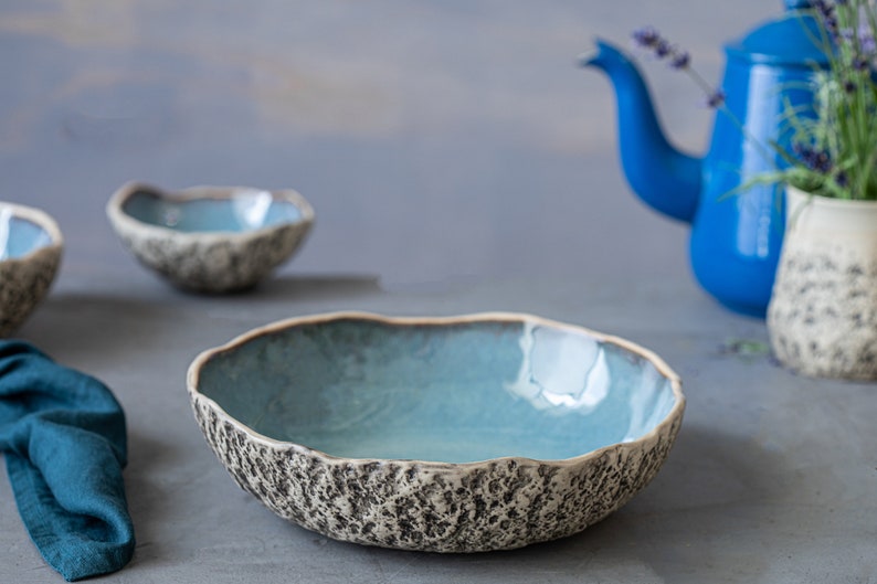 May include: A set of three blue and white ceramic bowls with a textured exterior. The bowls are arranged on a gray surface.