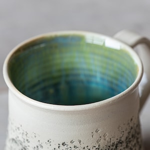 May include: A white ceramic mug with a speckled black glaze and a blue and green glazed interior.