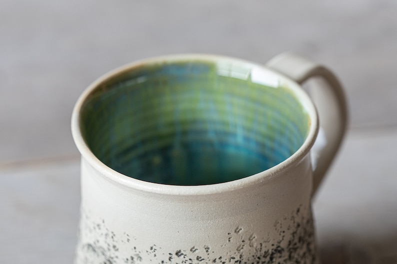 May include: A white ceramic mug with a speckled black glaze and a blue and green glazed interior.