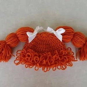 May include: A bright orange crocheted hat featuring two thick yarn pigtails on either side, each tied with a small white ribbon bow. The hat has a textured, looped fringe along the bottom edge, mimicking a hairstyle with bangs and side braids.