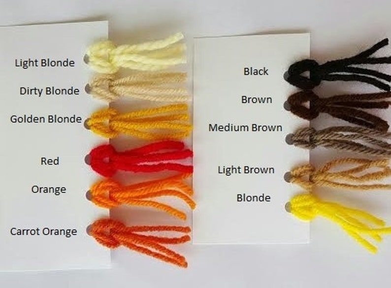 May include: A color chart featuring twelve yarn samples attached to two white cards. The left card lists Light Blonde, Dirty Blonde, Golden Blonde, Red, Orange, and Carrot Orange. The right card lists Black, Brown, Medium Brown, Light Brown, and Blonde.