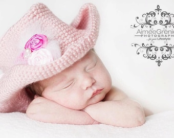 May include: A sleeping baby girl wearing a pink crocheted cowboy hat with a pink and white flower embellishment.