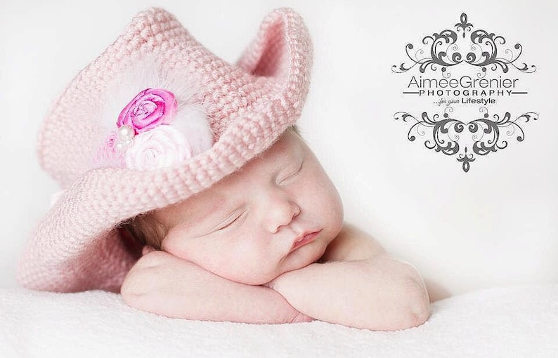 May include: A sleeping baby girl wearing a pink crocheted cowboy hat with a pink and white flower embellishment.