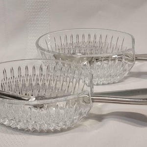 May include: Two clear glass bowls with a diamond pattern and silver handles. The bowls are ideal for serving snacks or desserts.