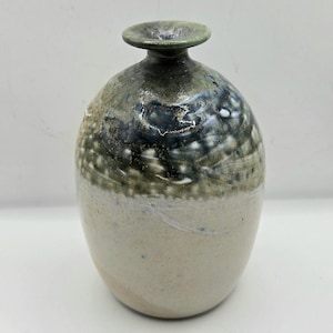 May include: A ceramic vase with a rounded body and a narrow neck featuring a flared rim. The upper portion of the vase displays a mottled dark blue and green glaze, while the lower section transitions into a smooth, light beige matte finish.