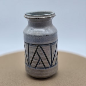 Può includere: Un piccolo vaso in ceramica bianca con un motivo geometrico blu e grigio. Il vaso ha un corpo arrotondato e un'apertura leggermente svasata.