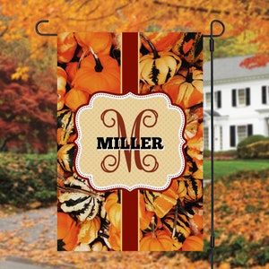May include: A fall-themed garden flag with a monogram "M" for Miller, surrounded by gourds and pumpkins in shades of orange, brown, and white. The flag has a red and white striped background.