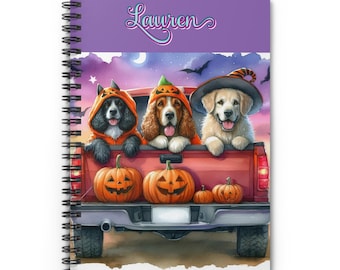 May include: A purple spiral bound notebook with the name "Lauren" on the cover. The cover features a red pickup truck with three dogs dressed in Halloween costumes. The dogs are wearing a witch hat, a pumpkin costume, and a black cat costume. The truck bed is filled with pumpkins.