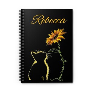 May include: Black spiral notebook with a black silhouette of a cat looking up at a yellow sunflower with the text "you are my sunshine" and the name "Rebecca" at the top.