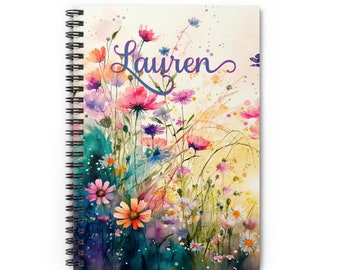 May include: A spiral bound notebook with a watercolor painting of a field of wildflowers. The name "Lauren" is written in purple cursive on the cover.
