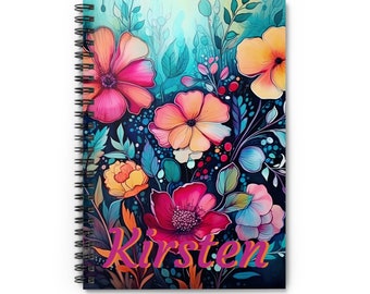 May include: A spiral bound notebook with a colorful floral design. The cover features pink, orange, yellow, and blue flowers on a dark blue background. The name "Kirsten" is written in pink cursive on the bottom of the cover.
