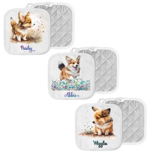 May include: Set of three white cotton pot holders with a quilted back. Each pot holder features a watercolor illustration of a corgi dog with a personalized name. The names are "Paisley", "Abbie", and "Wiggles".