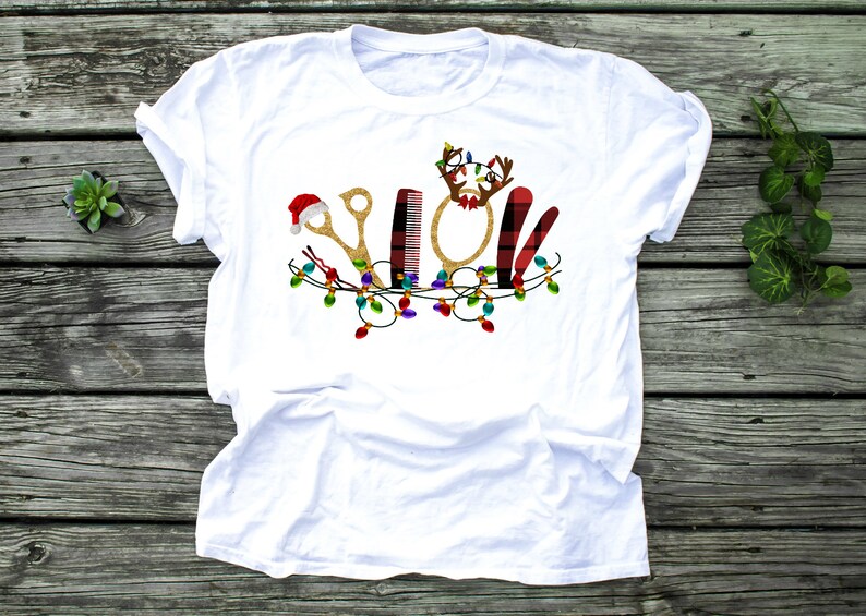 May include: White t-shirt with a Christmas-themed design featuring a pair of gold scissors, a comb, a round mirror, a red and black plaid hair cutting tool, and a Santa hat. The design is surrounded by a string of colorful Christmas lights.