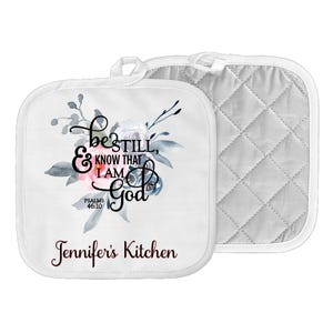 May include: White kitchen pot holders with a floral design and the text "Be still, & know that I am God, Psalms 46:10" and "Jennifer's Kitchen".