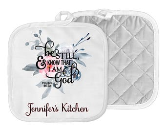 May include: White kitchen pot holders with a floral design and the text "Be still, & know that I am God, Psalms 46:10" and "Jennifer's Kitchen".