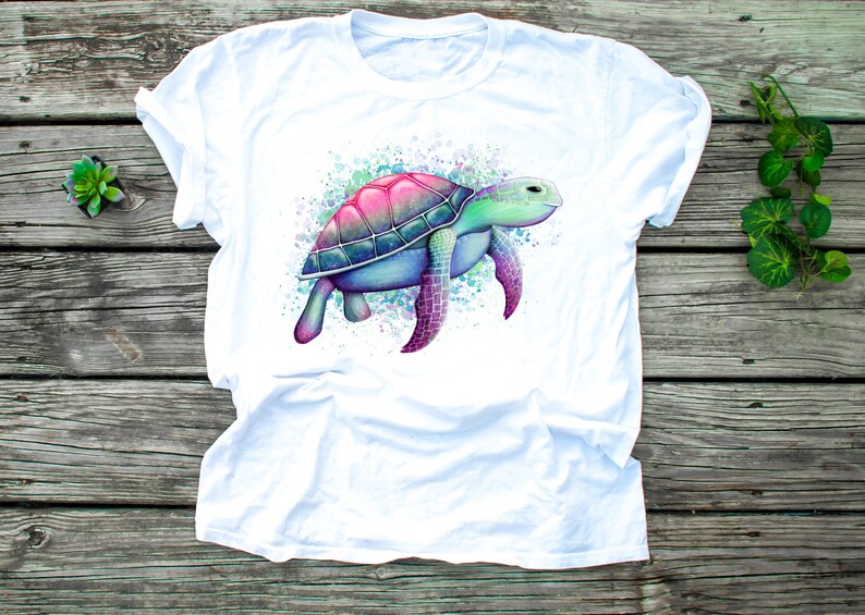 May include: White t-shirt featuring a watercolour illustration of a sea turtle in shades of pink, blue and green.