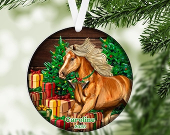 May include: Circular Christmas ornament depicting a brown horse with a flowing mane, surrounded by wrapped gifts and Christmas trees. The ornament has the name "Caroline" and the year "2025" printed on it. A white ribbon is attached for hanging.