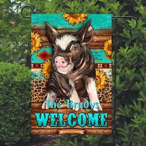 May include: A welcome garden flag with a cute piglet in the center. The flag has a turquoise background with a wooden plank design and sunflowers. The text "The Bradys WELCOME" is printed on the flag.