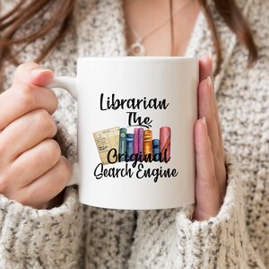 May include: White ceramic mug with a black design that reads "Librarian The Original Search Engine". The design also includes a stack of colorful books and a card with writing on it.