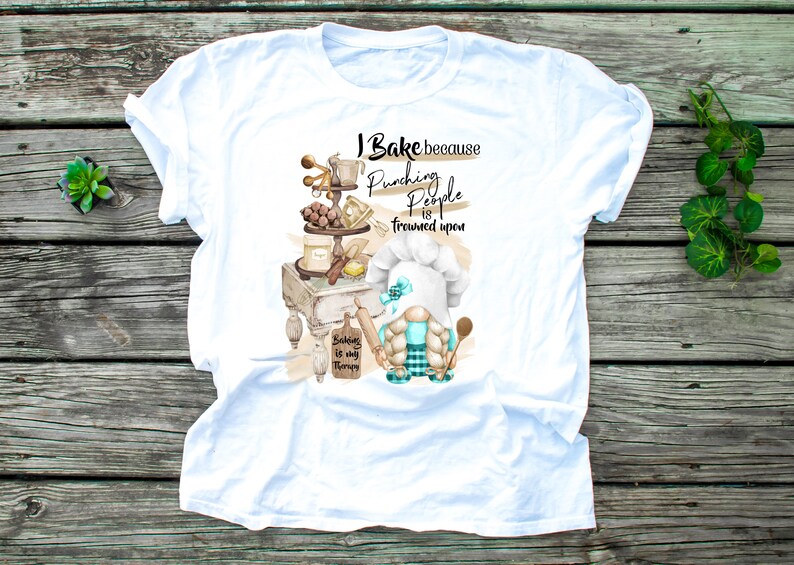 May include: White t-shirt with a baking-themed graphic. The design features a gnome chef, baking tools, and the text "I Bake because punching people is frowned upon. Baking is my therapy."
