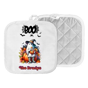 May include: White Halloween pot holder with a ghost wearing a witch hat and holding a pumpkin. The pot holder has the word "BOO" with spiderwebs and bats, and the name "The Bradys" in pink.